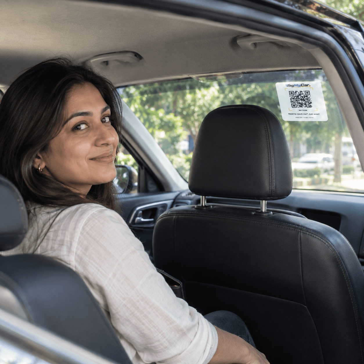 Anjali, a TagMyCar customer, looking back from the driver's seat with the tag on the rear windshield