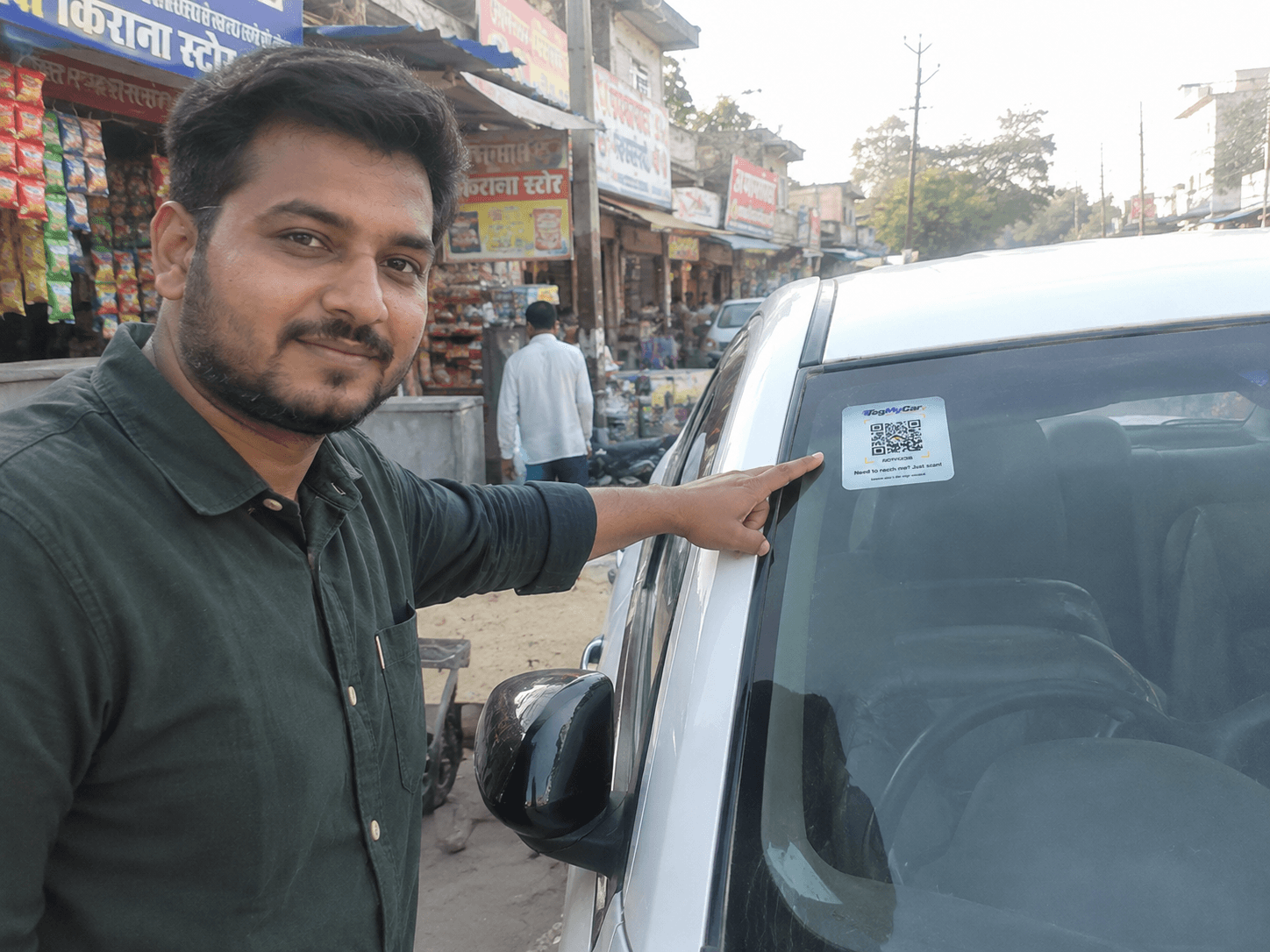 Chander, a TagMyCar customer, pointing at the TagMyCar QR tag pasted on his car's rear window in a market street